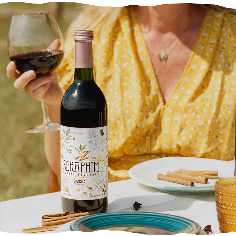 Bottles of Seraphim Social Beverage, a non-alcoholic social wine alternative made from pure ingredients. Featured flavors in image: a bottle of Cassia and Cacao with a poured clear glass.