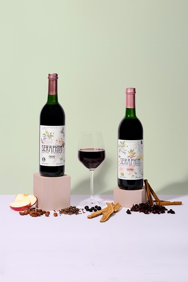 Bottles of Seraphim Social Beverage, a non-alcoholic social wine alternative made from pure ingredients. Featured flavors in image: a bottle of Cassia and Cacao with a poured clear glass. Social non alcoholic drinks for wellness