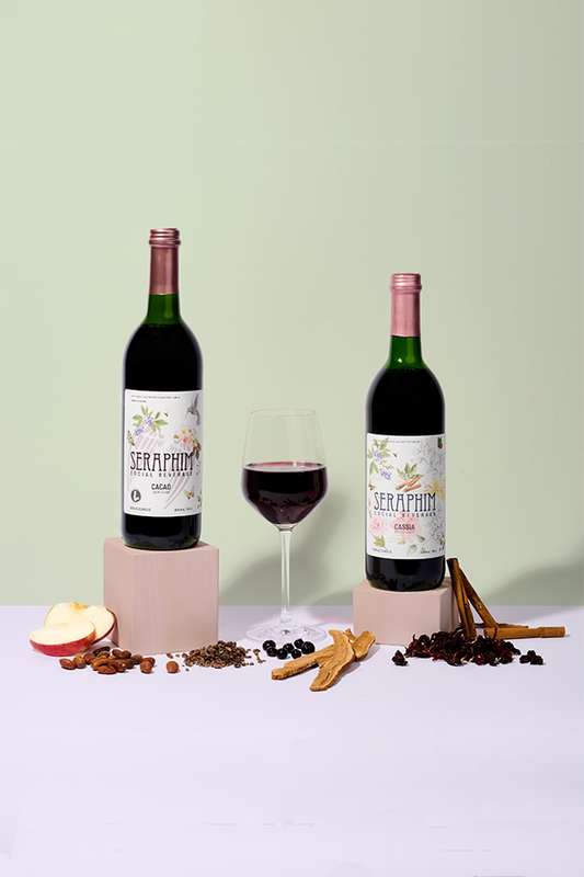 Bottles of Seraphim Social Beverage, a non-alcoholic social wine alternative made from pure ingredients. Featured flavors in image: a bottle of Cassia and Cacao with a poured clear glass.  Social non alcoholic drinks for wellness